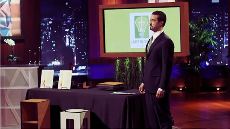 Jared Joyce standing beside his Five Minute Furniture prototypes on Shark Tank, with his logo displayed on a screen behind him.