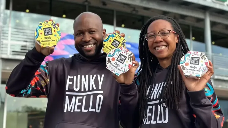 Funky Mello founders Delisa and Zach Harper holding up various flavors of their marshmallow crème outside a modern building, both wearing branded hoodies.