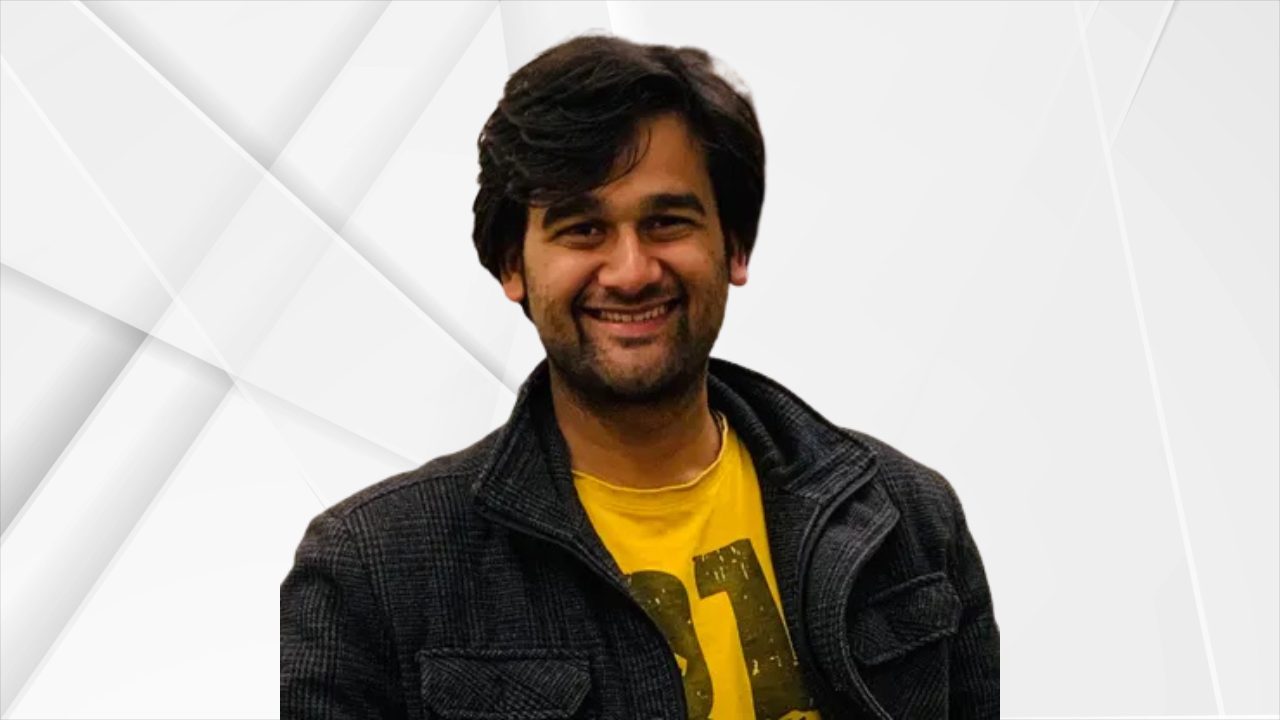 A smiling Gulshan Sharma, founder of Falhari, wearing a black jacket over a yellow t-shirt, posing against a white geometric background.