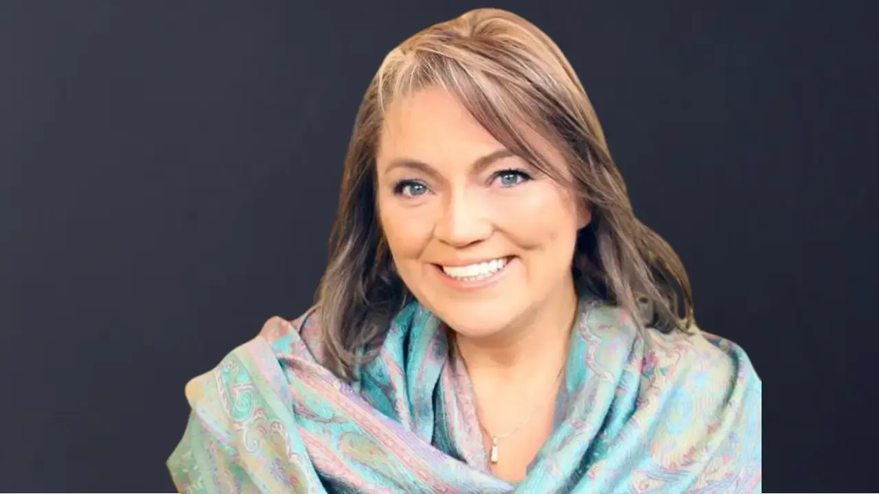 Jen Lawrence, founder of newagestore.com, smiling in a professional portrait with a dark background, wearing a patterned shawl.