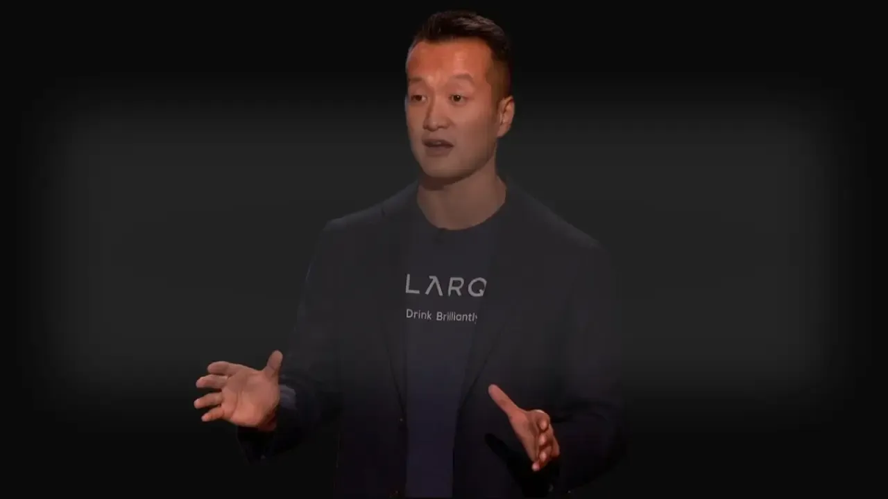 Justin Wang, CEO of LARQ, pitching his self-cleaning water bottle on Shark Tank, wearing a LARQ-branded shirt and blazer.