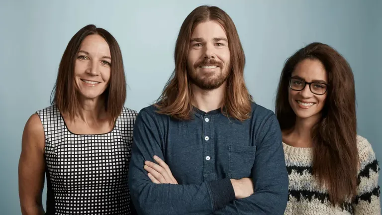 Dan Price, CEO of Gravity Payments, standing with two employees after taking a 94% pay cut to raise employee salaries to $70K.