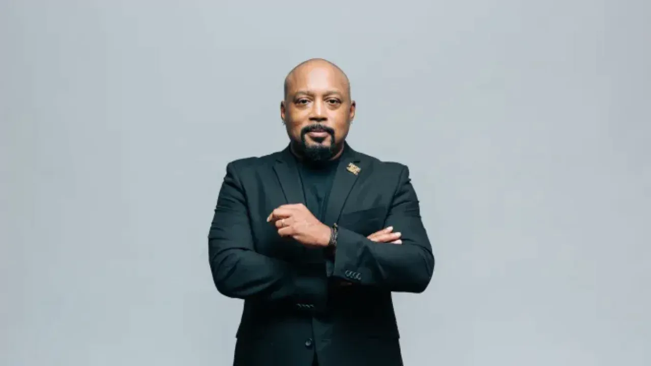 Daymond John standing confidently in a black suit, sharing daily habits of successful entrepreneurs.