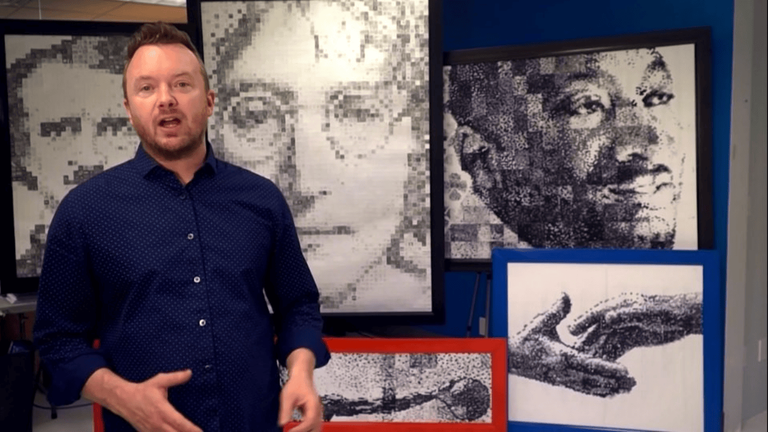 Phil Hansen standing in his studio surrounded by portraits he created using unconventional art techniques.