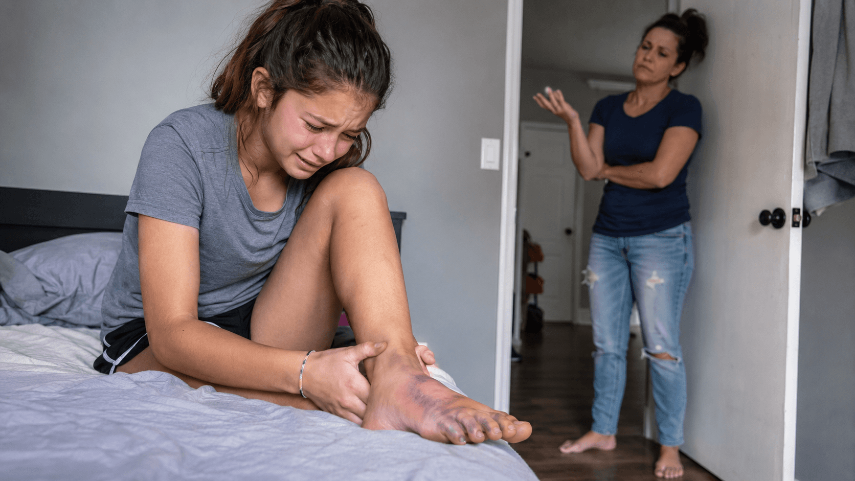 Teen girl crying over injured foot while her mother dismisses her pain.