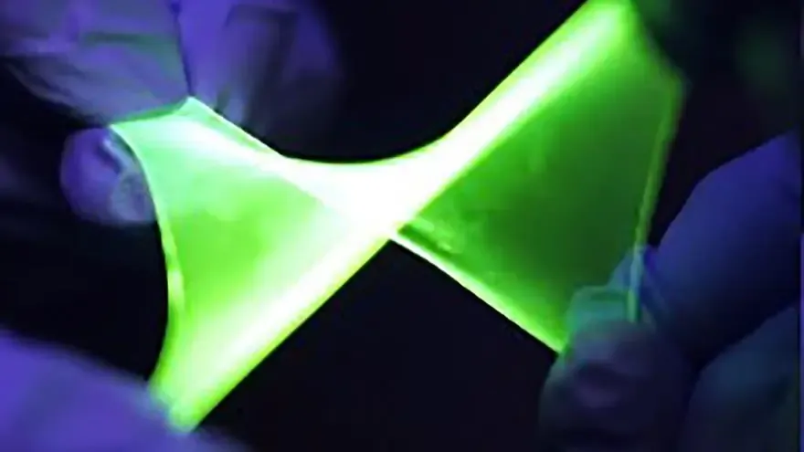 Flexible green OLED display glowing while being gently bent between gloved hands in a laboratory setting.